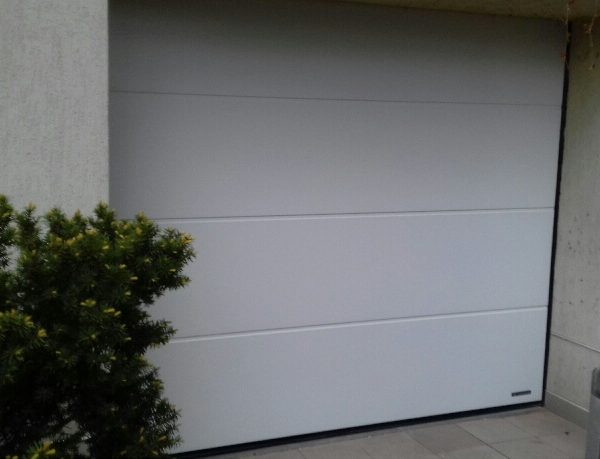 Brama segmentowa bez przetłoczeń w białym kolorze, nadająca budynkowi elegancki, minimalistyczny wygląd.