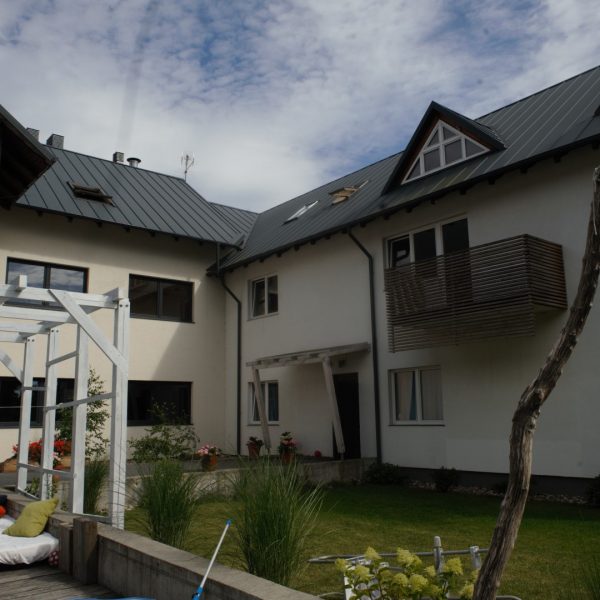 Nowoczesny budynek mieszkalny z jasną elewacją i ogrodem, pokryty blachą na rąbek stojący Pruszyński w kolorze grafitowym – trwałe i estetyczne pokrycie dachowe idealne do współczesnych projektów