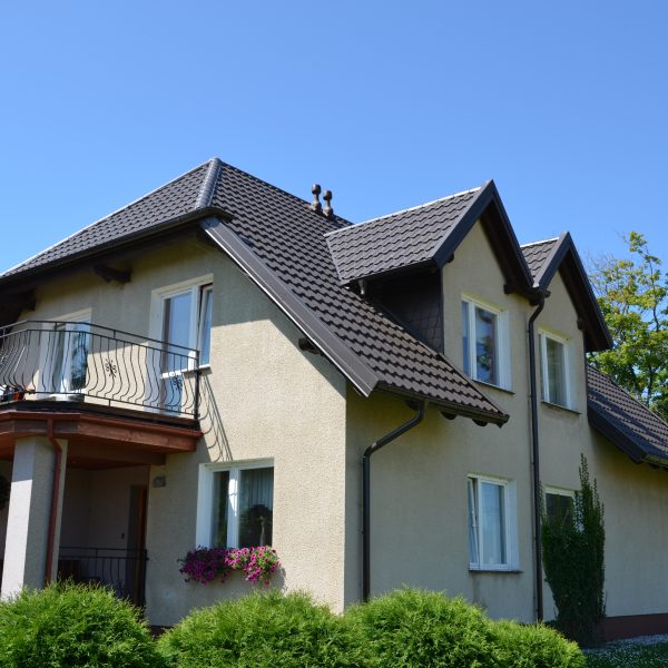 Dom jednorodzinny z dachem pokrytym blachodachówką modułową Ruukki Finnera w kolorze brązowym. Dach ma nowoczesny wygląd z widocznym połyskiem i zintegrowanym systemem rynnowym.