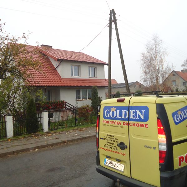 Dwupiętrowy dom z jasną elewacją i dachem pokrytym blachodachówką Ruukki Finnera w kolorze ceglastym, z balkonem ozdobionym kwiatami oraz ogrodzeniem z przodu.