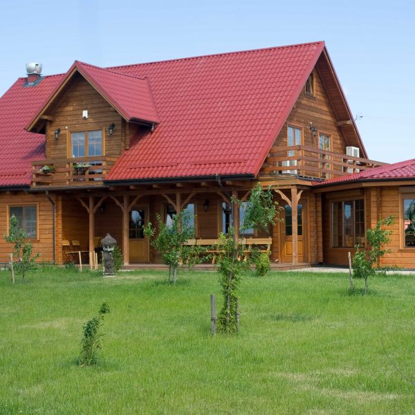 Drewniany dom z dachem z blachodachówki Ruukki Monterrey w kolorze wiśniowym – eleganckie połączenie czerwonego dachu z naturalną elewacją z drewna, idealne do stylu góralskiego i wiejskiego.