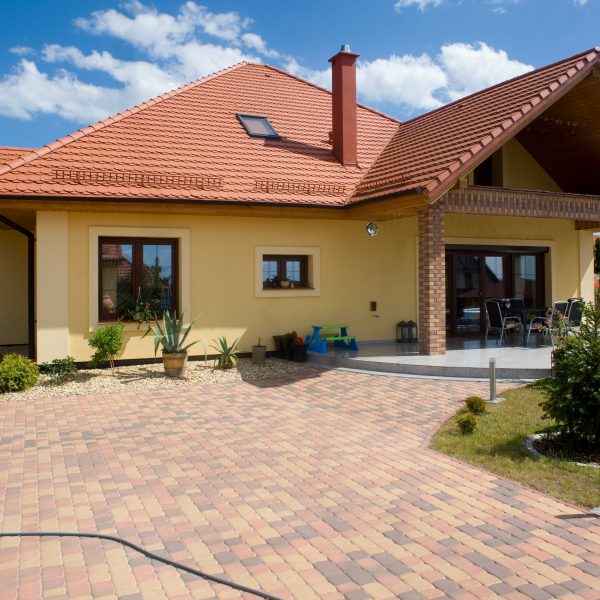 Dach z dachówki Wienerberger karpiówka Natura na domu z żółtą elewacją i stylowym podjazdem z kostki brukowej