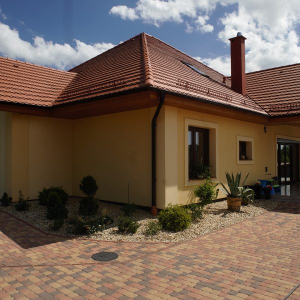 Dach z dachówki Wienerberger karpiówka Natura na domu z żółtą elewacją i stylowym podjazdem z kostki brukowej