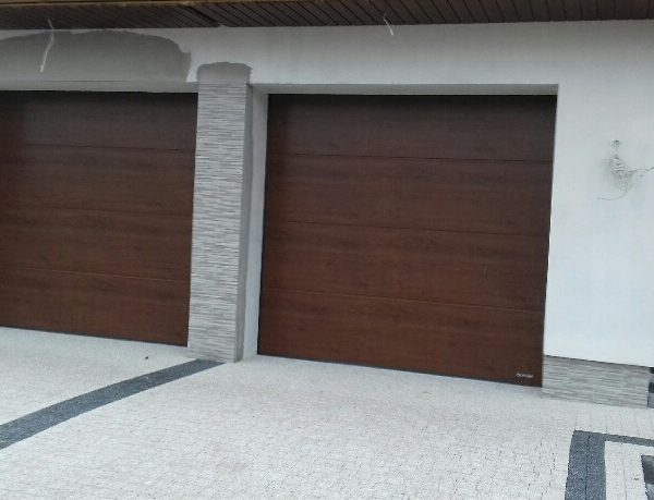 Dwie bramy garażowe w spójnym wykończeniu, estetycznie wkomponowane w architekturę domu.
