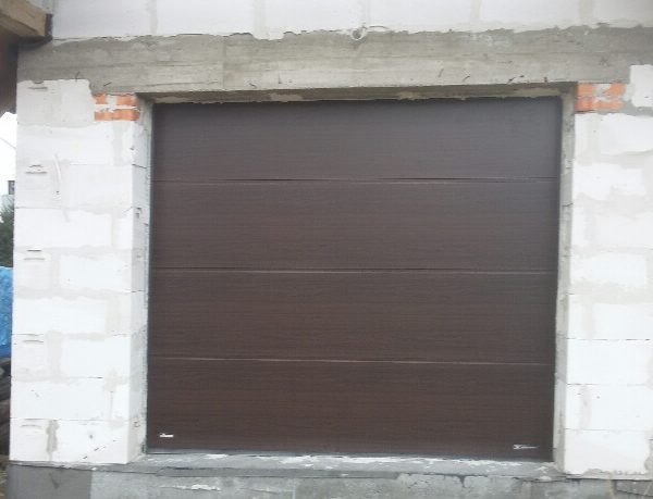 Realizacja z gładką bramą segmentową w odcieniu brązu, harmonizującą z tradycyjną architekturą.