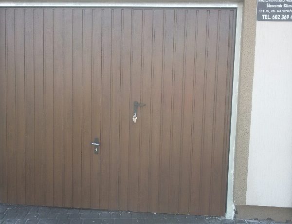 Brama uchylna w kolorze orzech, elegancko wkomponowana w elewację budynku.