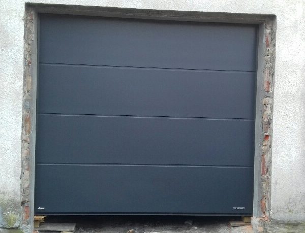 Realizacja z gładką bramą segmentową w odcieniu antracytu, harmonizującą z minimalistyczną elewacją.