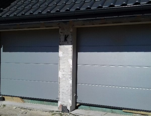 Realizacja z dwiema gładkimi bramami segmentowymi, tworzącymi spójną, nowoczesną fasadę.